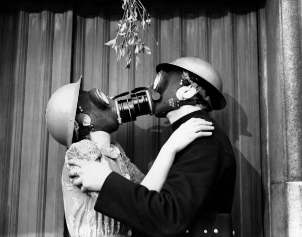 A couple kissing under a mistletoe, with gas masks on.